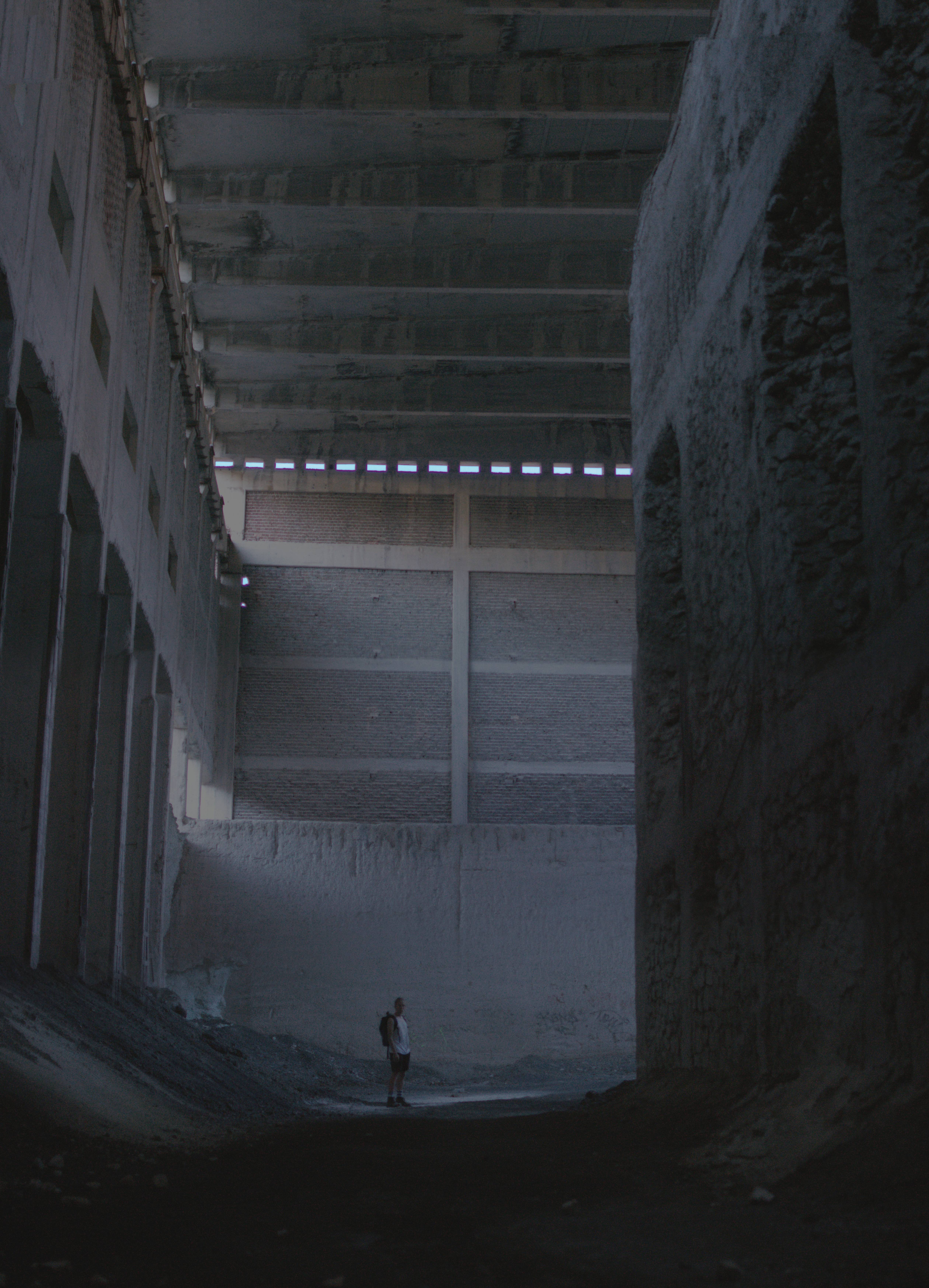 Dude standing inside huge concrete room, moody lighting